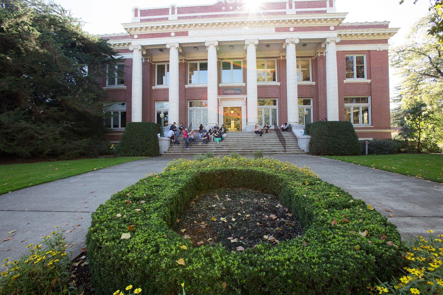 Landscaped Oregon "O" in front of Johnson hall, a red brick building with white front columns.