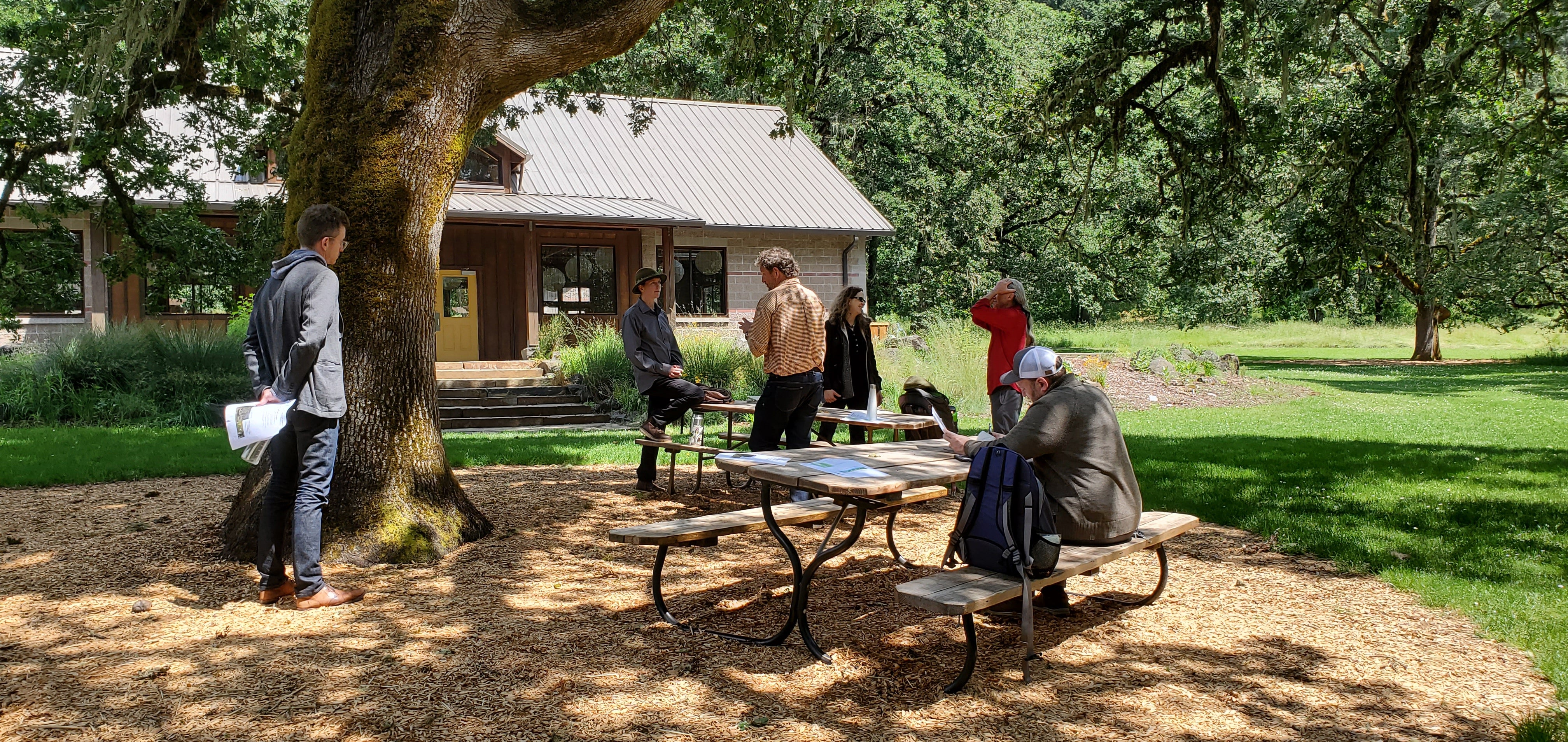 UO faculty talk with a community partner under a large oak tree at Mount Pisgah arboretum