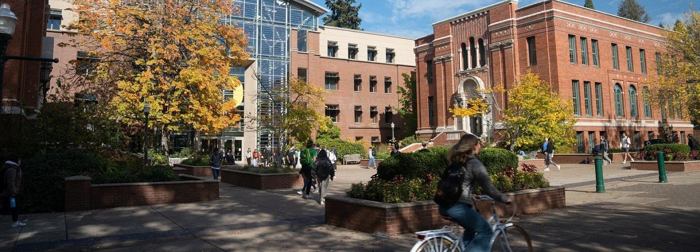 Pedestrians and cyclists travel on the west side of University of Oregon campus on a sunny day