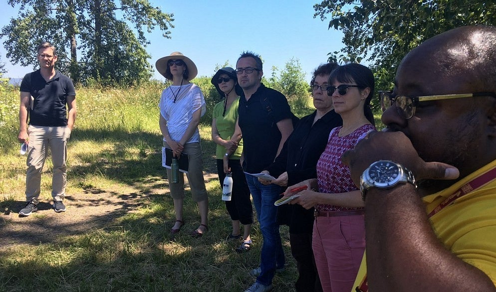 UO faculty hear from a community partner in an outside area with trees and grass.