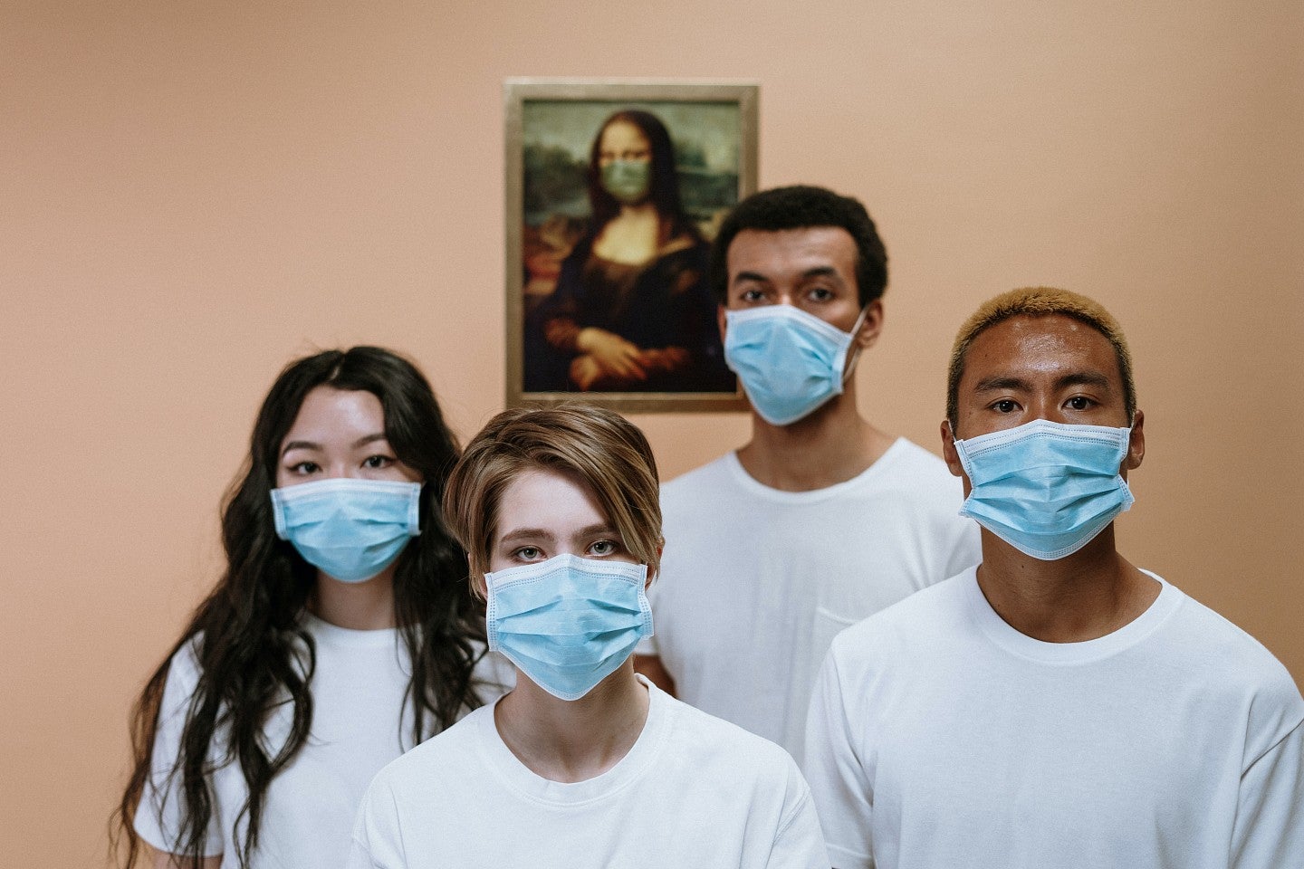 Young people wearing masks in front of a picture of the Mona Lisa, also wearing a mask.
