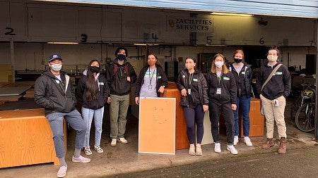 Multiple student workers stand around available surplus office furniture.