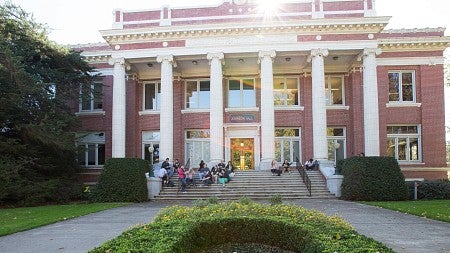 Students sit on the steps of Johnson Hall, a red brick building with white columns.